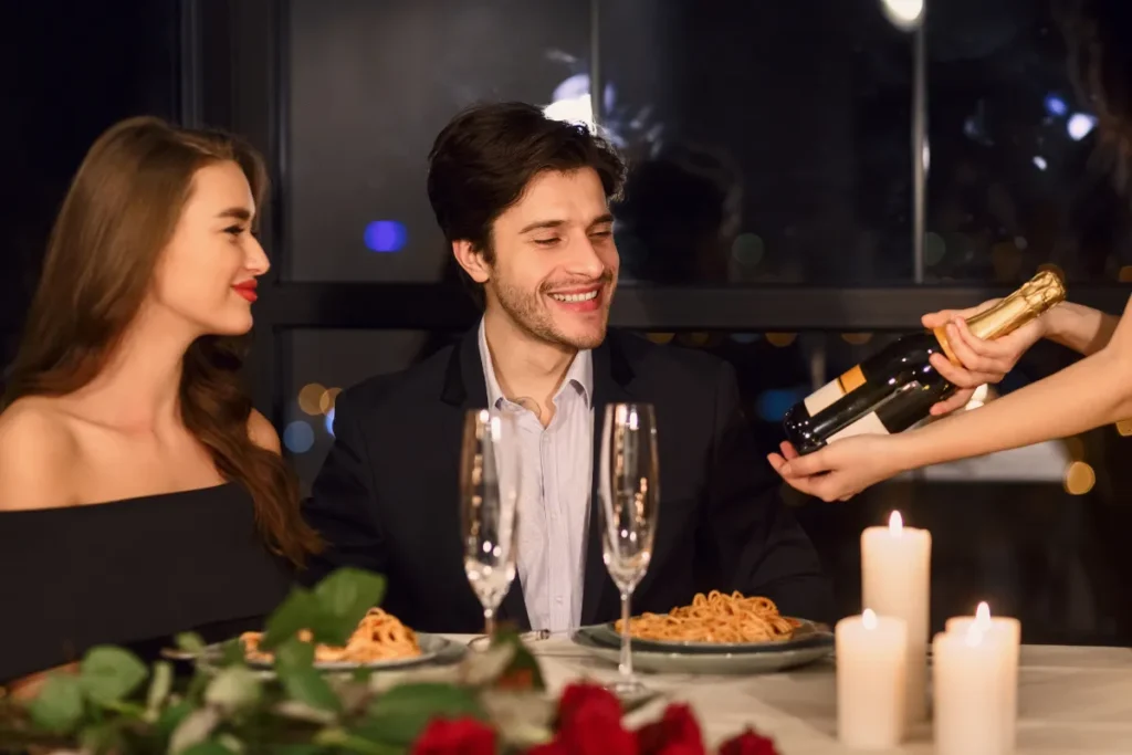 Casal jantando à noite enquanto garçom serve vinho em mesa com velas