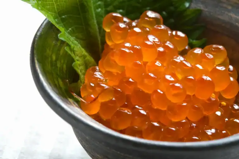 Ovas de peixe alaranjadas servidas em cumbuca com folha verde ao fundo