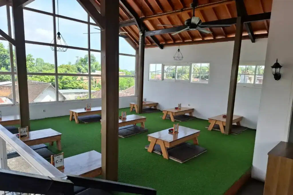 salão de restaurante com janelas grandes, vista elevada e mesas baixas em ambiente iluminado