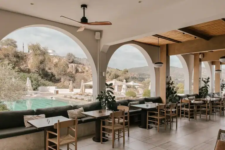 restaurante com mesas próximas a janelas amplas com vista para área externa com piscina e natureza