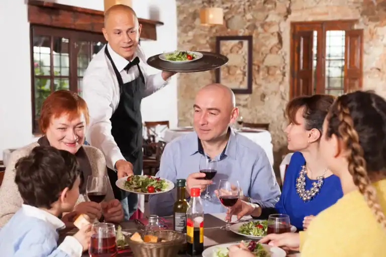Garçom servindo pratos para família reunida à mesa em restaurante de Florianópolis