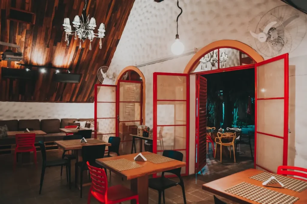 Salão de restaurante com portas vermelhas abertas, mesas organizadas e iluminação interna em Santo Antônio de Lisboa