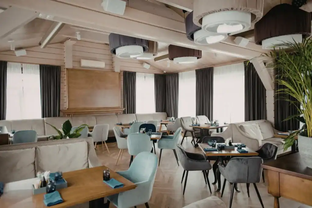 salão interno de restaurante com mesas organizadas, cadeiras estofadas e iluminação decorativa