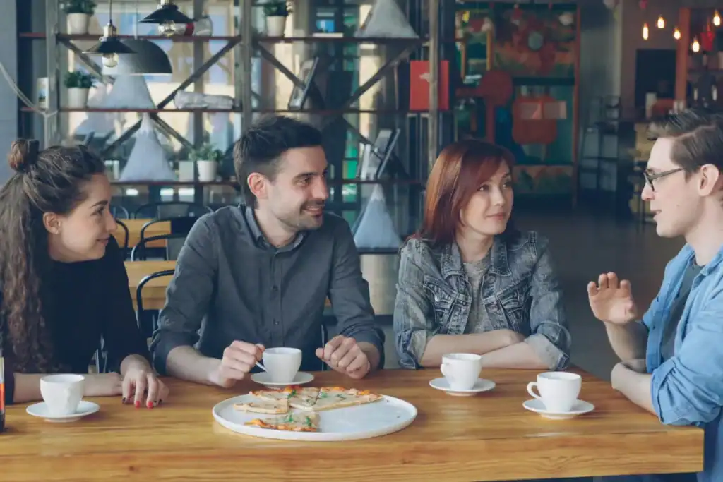 grupo de amigos conversando em mesa de restaurante com pizza e xícaras de café