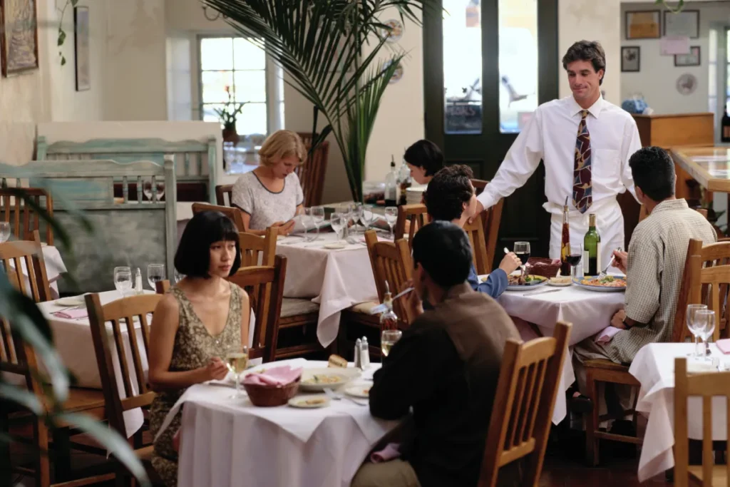 pessoas sentadas em mesas de restaurante com garçom atendendo em ambiente interno
