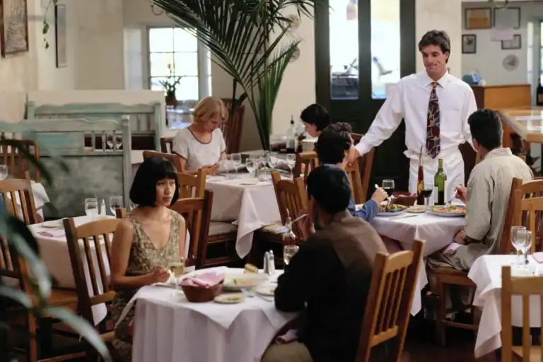 pessoas sentadas em mesas de restaurante com garçom atendendo em ambiente interno