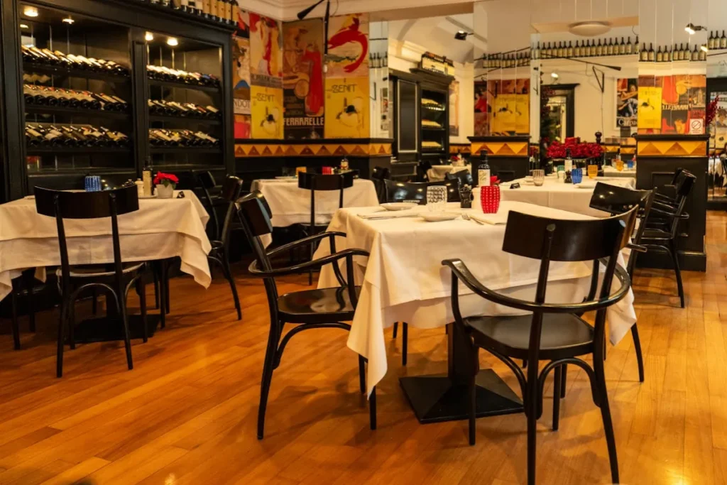 Interior de restaurante com mesas organizadas, toalhas brancas e adega de vinhos ao fundo no Campeche em Florianópolis
