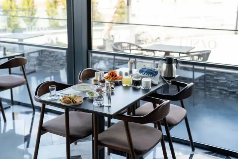 Mesa de café da manhã com pães, bebidas e pratos servidos próxima a uma janela em restaurante no Campeche em Florianópolis
