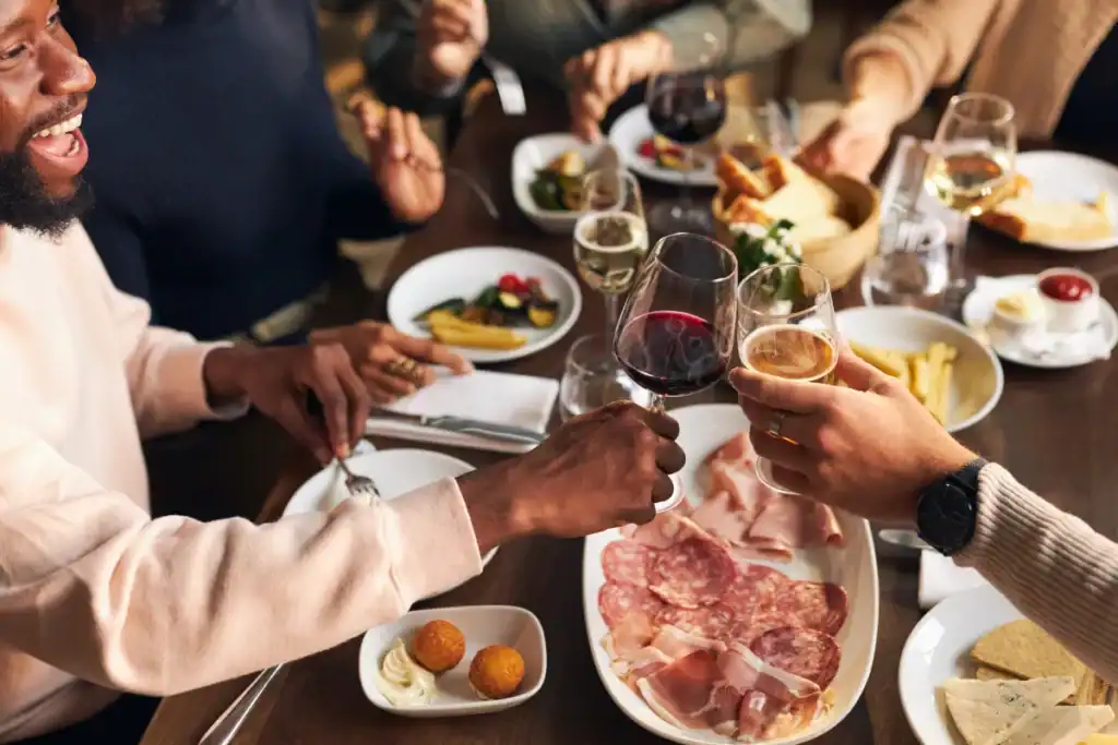 Pessoas brindando com taças de vinho em uma mesa cheia de pratos durante um jantar comemorativo