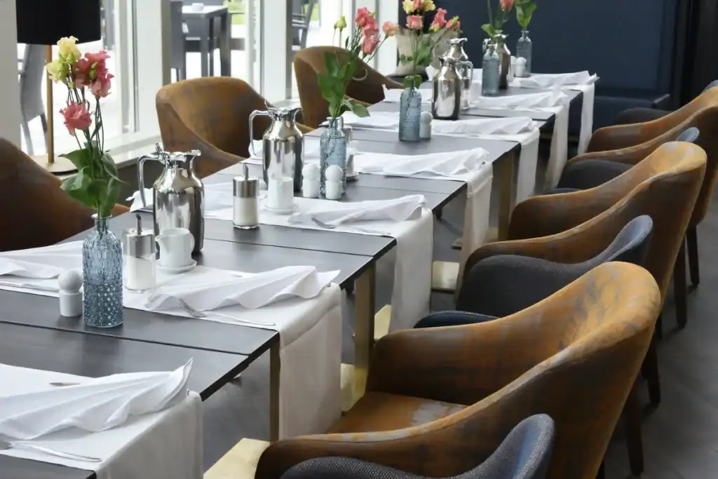 Restaurantes para aniversário Florianópolis. Mesas organizadas com toalhas, flores e utensílios em um restaurante elegante com cadeiras confortáveis
