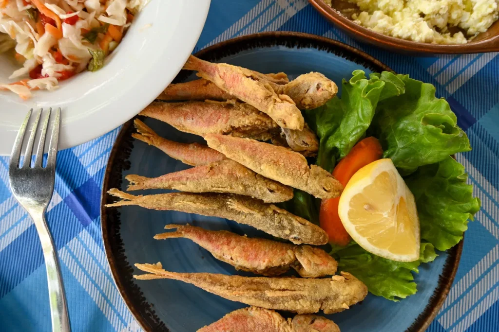 Peixes pequenos fritos inteiros servidos com limão, salada e acompanhamentos