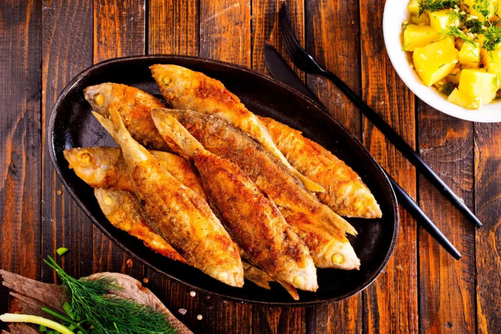 Tainha em Florianópolis. Peixes assados inteiros servidos em travessa sobre mesa de madeira com acompanhamentos