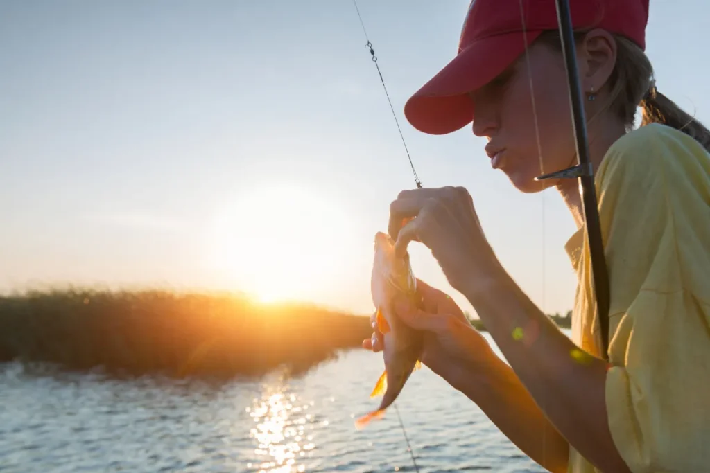 Temporada da tainha Florianópolis. Pessoa segurando peixe recém pescado ao pôr do sol próximo à água