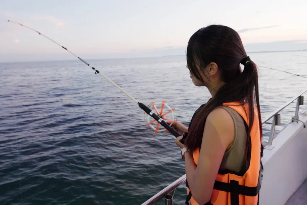 mulher pescando com vara em um barco no mar usando colete salva-vidas