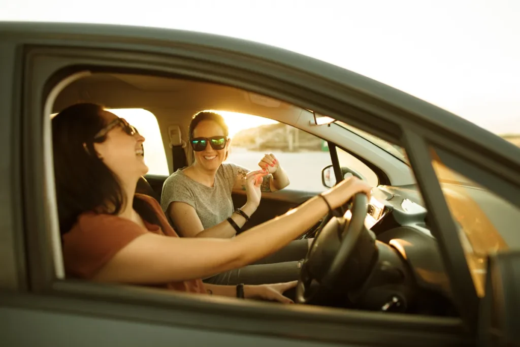 duas mulheres sorrindo dentro do carro durante viagem com luz do pôr do sol, representando trajeto entre Curitiba e Florianópolis