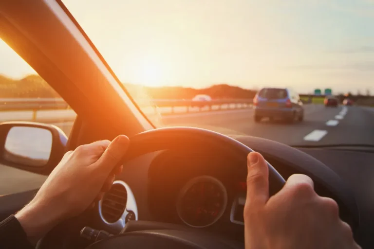 Mãos no volante dirigindo em rodovia ao pôr do sol, representando viagem de carro entre Florianópolis e Joinville pela BR-101