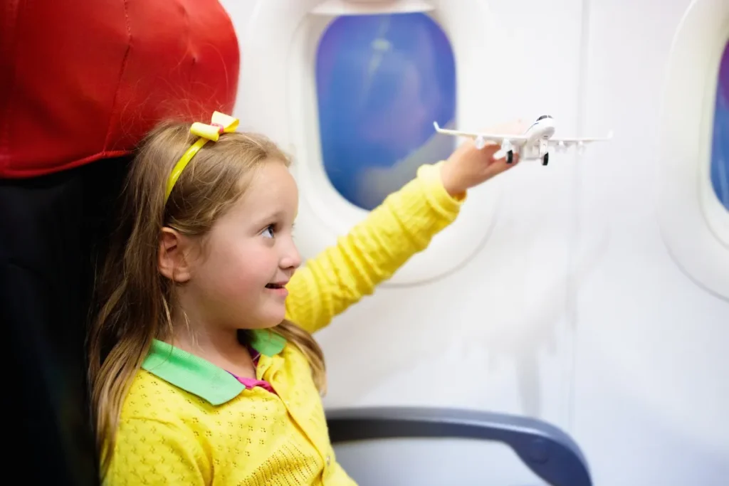 criança sentada em avião segurando brinquedo de avião perto da janela, representando experiência de voo para Florianópolis
