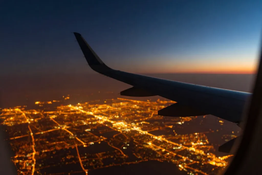 vista aérea noturna de cidade iluminada através da janela do avião, mostrando trajeto aéreo rumo a Florianópolis