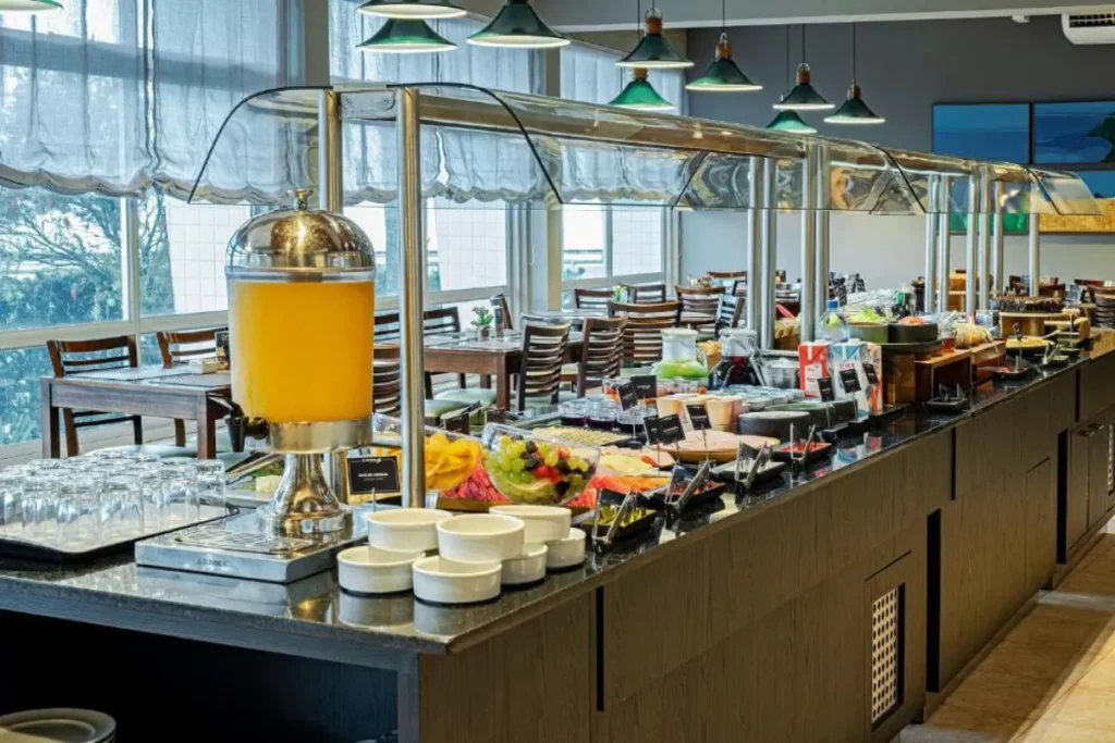 Buffet de café da manhã do Hotel Slaviero Baía Norte com frutas, bebidas e área interna moderna em Florianópolis
