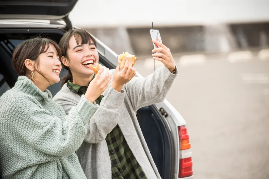 Mulheres tirando selfie ao lado de carro estacionado na Beira-Mar Norte durante passeio em Florianópolis.