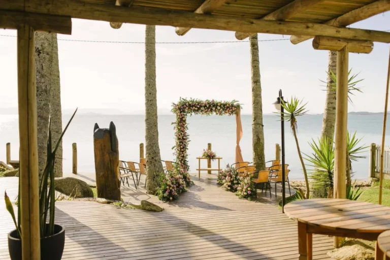 Cerimônia ao ar livre no Coco Beach Floripa com arco floral, deck de madeira e vista para o mar em Florianópolis