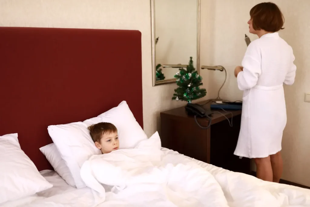 Melhores hotéis para crianças em Florianópolis. Criança descansando em cama de hotel enquanto adulta se prepara no quarto de hospedagem familiar
