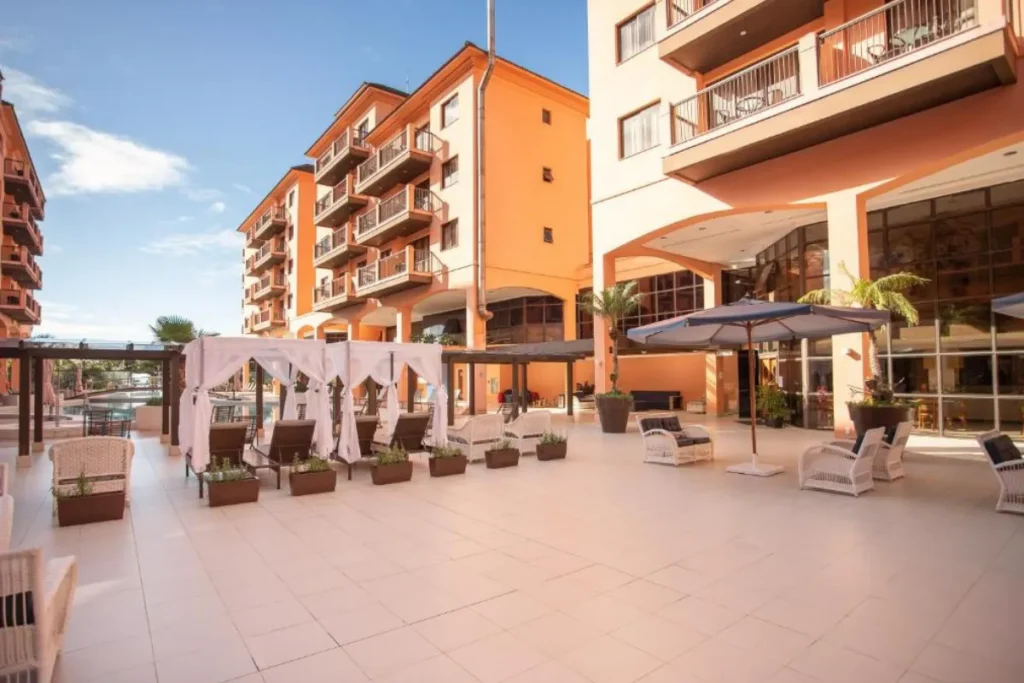 Área comum do Jurerê Beach Village com lounges, ombrelones e fachada moderna em Jurerê Internacional.