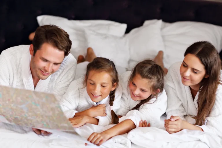 Família com duas crianças reunida na cama de hotel analisando mapa durante hospedagem em Florianópolis