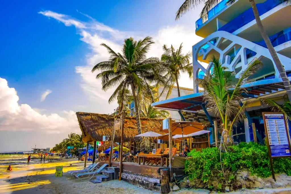 Hotel próximo à praia com restaurantes, coqueiros e movimento turístico em região costeira famosa