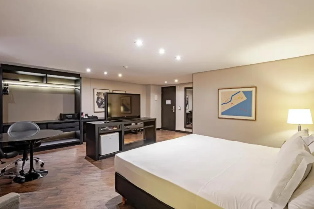 Quarto amplo do Hotel Slaviero Baía Norte com cama casal, televisão e espaço de trabalho em Florianópolis