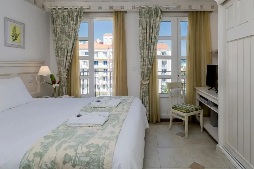 Suíte confortável do IL Campanario com decoração clássica, cama de casal e varanda em Jurerê Internacional.