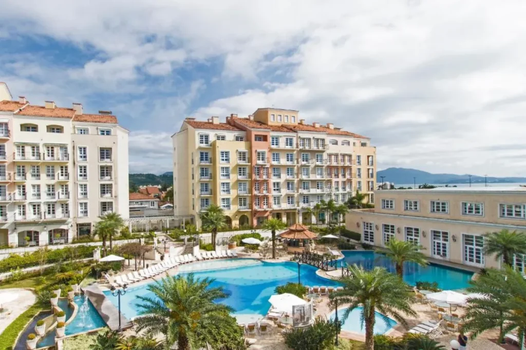Área externa do IL Campanario com piscinas amplas, espreguiçadeiras e prédios em estilo europeu em Jurerê.