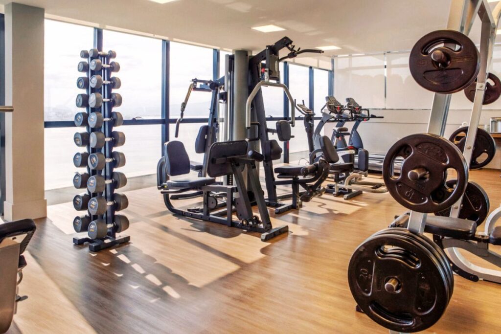 Academia moderna com aparelhos de musculação, halteres, esteiras e anilhas em ambiente iluminado.