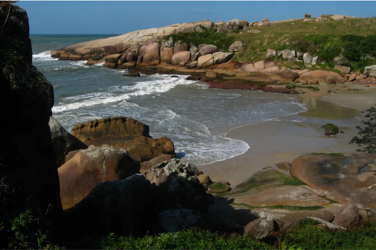Faixa de areia da Praia do Gravatá cercada por costões e vegetação