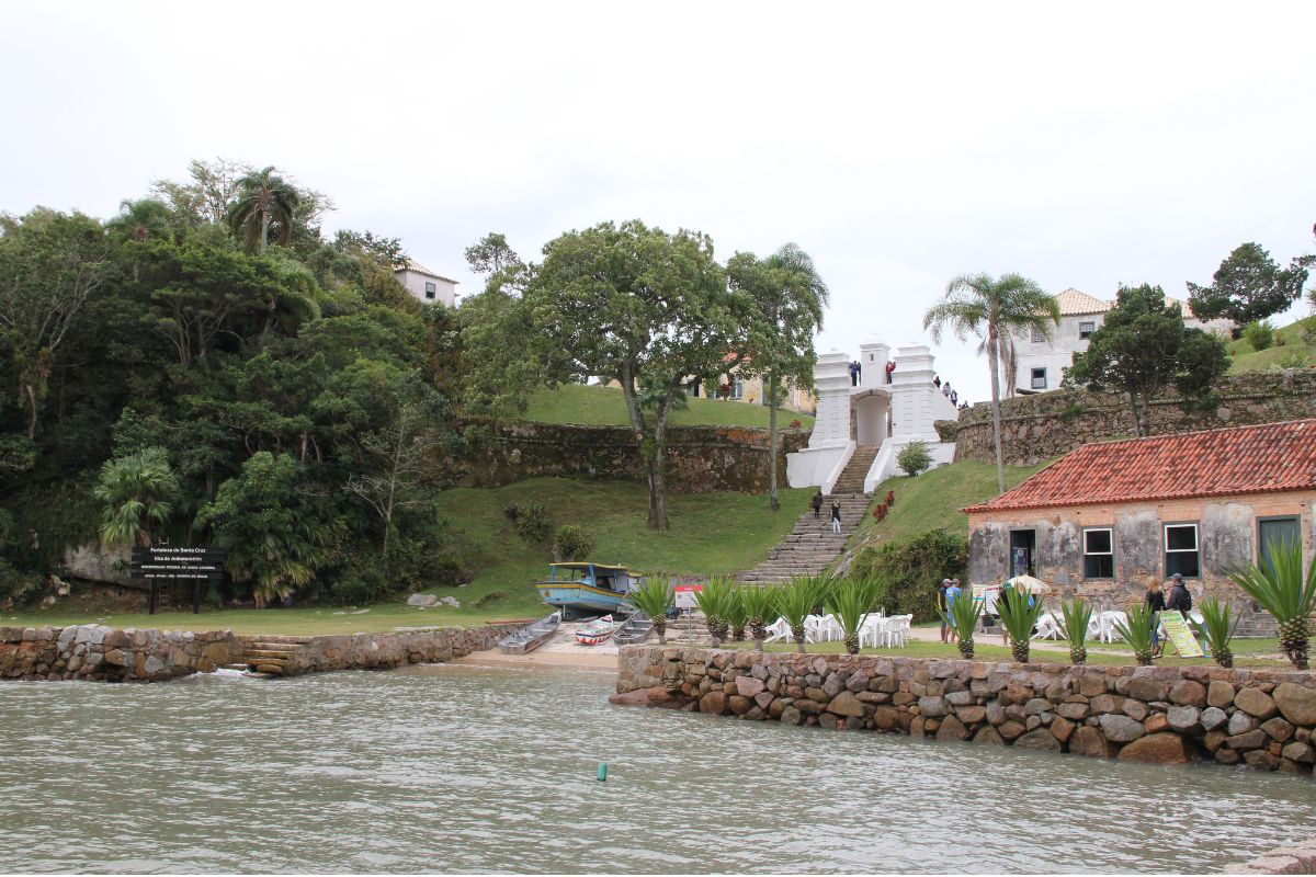Chegada de barco à Fortaleza de Santa Cruz de Anhatomirim com o conjunto histórico ao fundo