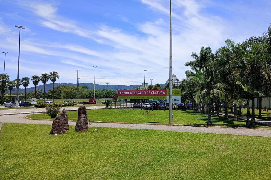 Área externa do Centro Integrado de Cultura de Florianópolis com gramado, palmeiras, estacionamento e placa de identificação.