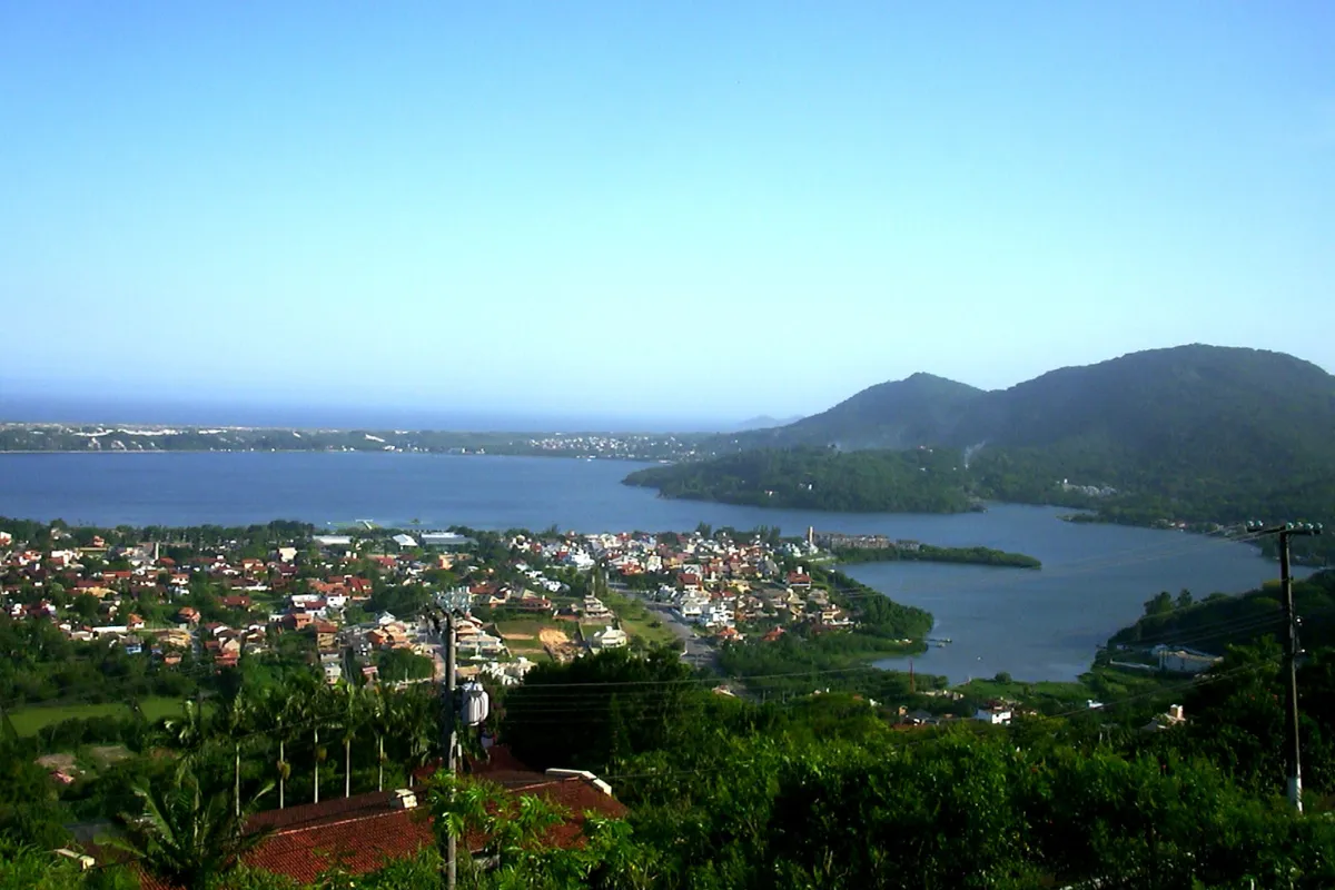 Vista elevada da Lagoa da Conceição, em Florianópolis, cercada por morros e áreas urbanizadas.