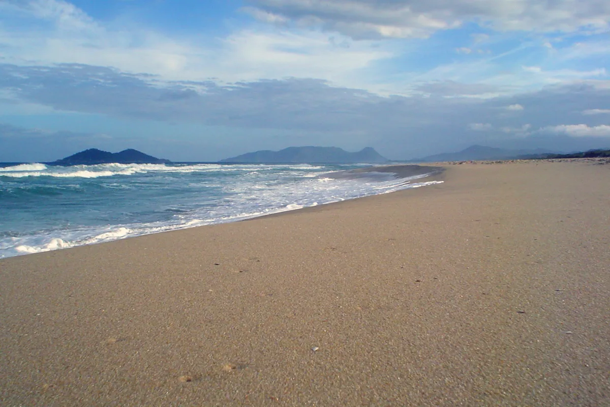 Praia do Campeche, em Florianópolis, com extensa faixa de areia e ondas no mar.