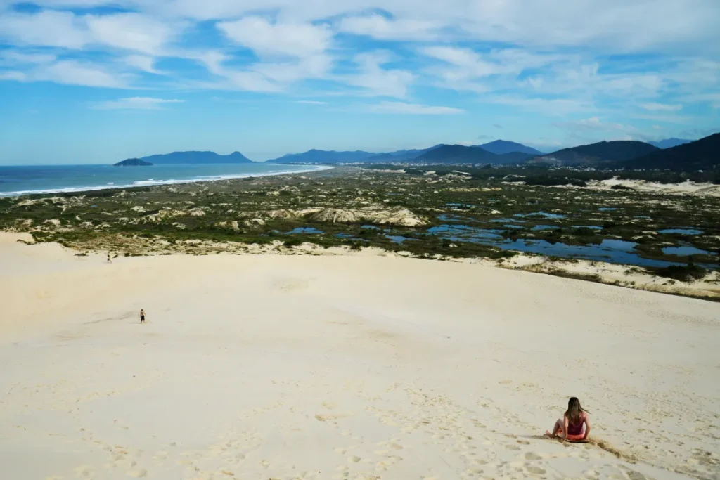 Grandes dunas de areia com vista para o litoral e montanhas na região da Lagoa da Conceição, em Florianópolis.