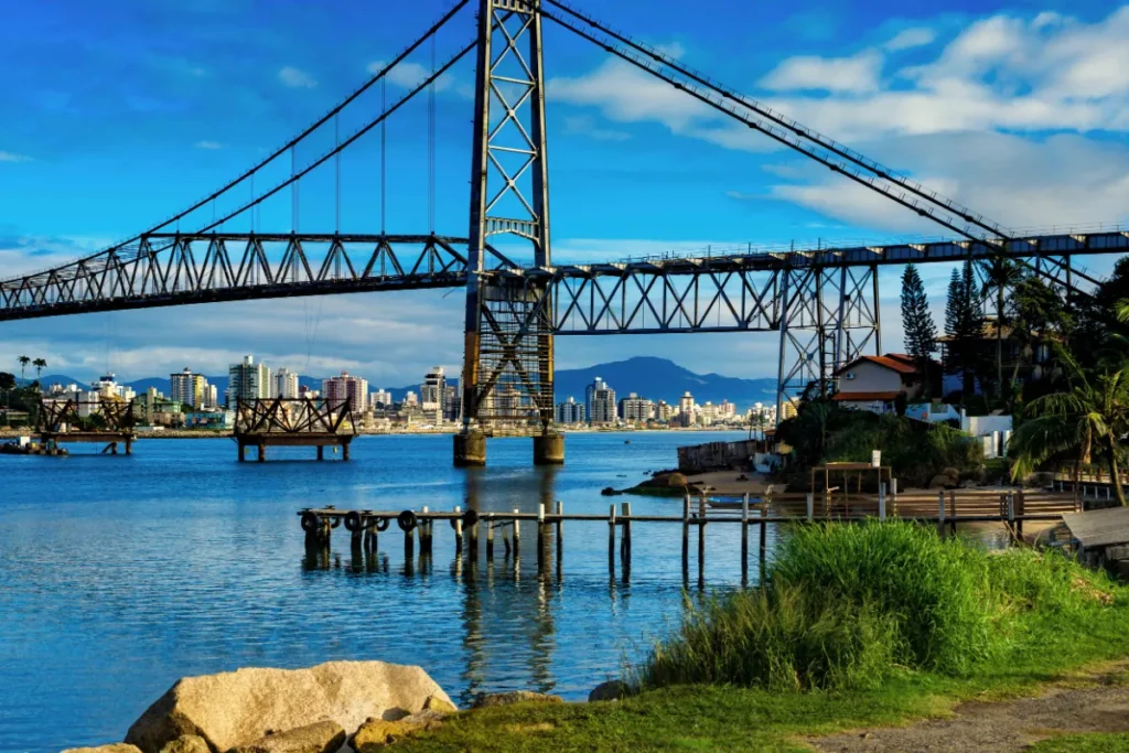 Vista da Ponte Hercílio Luz a partir do Parque da Luz, com o mar e prédios de Florianópolis ao fundo.
