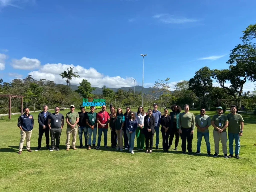 Servidores do IMA e da Floram posam em gramado diante de letreiro de jardim botânico, com morros ao fundo