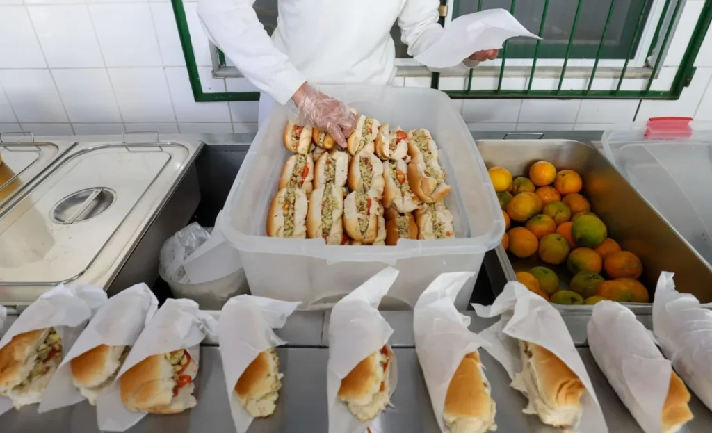 Merendeira organiza lanches embalados e caixa de laranjas na cozinha de uma escola estadual de Santa Catarina