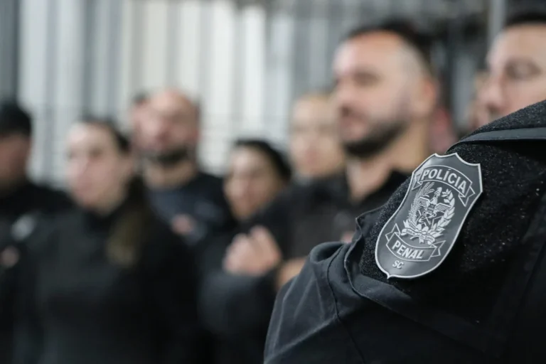 Policiais penais de Santa Catarina perfilados, com o brasão da Polícia Penal no uniforme em primeiro plano